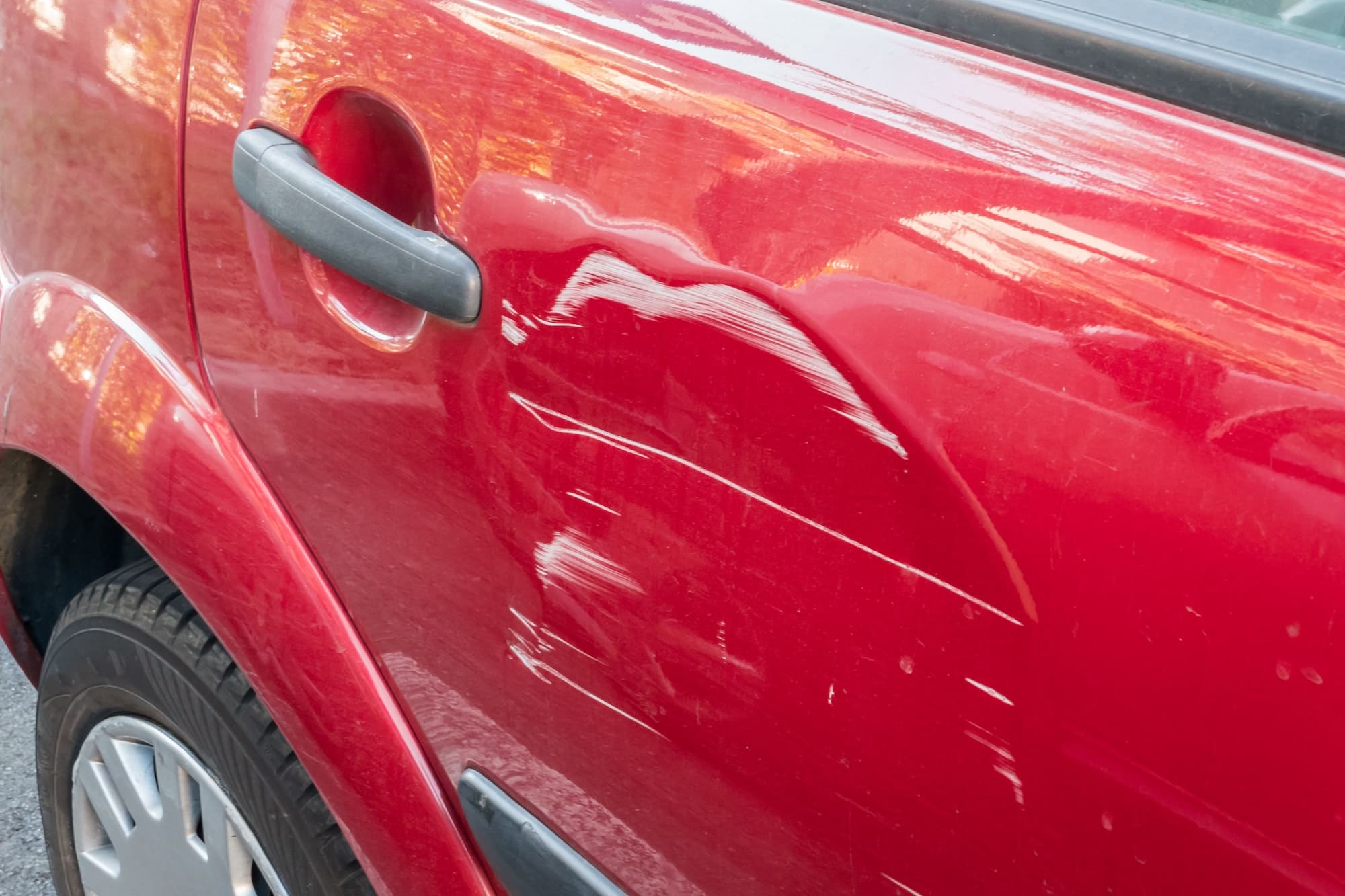 Scratches on the side door of the red car. Collision or accident.