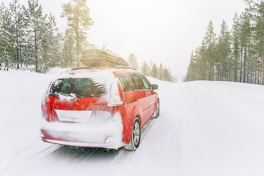 Red car with roof box on winter snow road. Snow winter forest with car on the road.