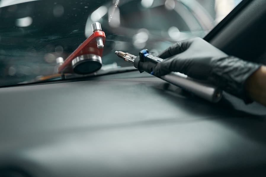 Gloved hand with windscreen repair drill lying on dashboard cover